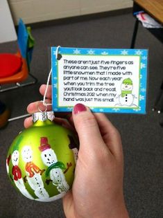 a hand holding a green ornament with snowmen on it and a poem