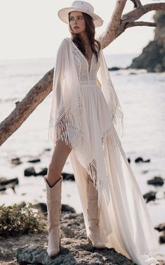 a woman standing on top of a rocky beach next to the ocean wearing a white hat