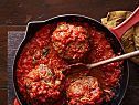 meatballs covered in marinara sauce in a skillet next to a wooden spoon