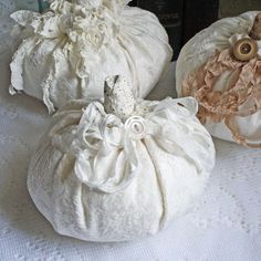 three white pumpkins sitting on top of a table covered in lace and fabric flowers