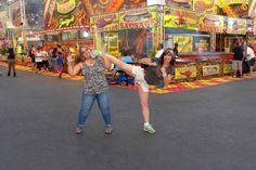 two women are dancing in front of carnival booths