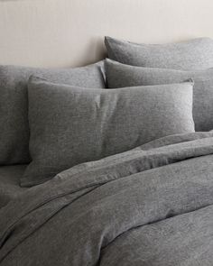 an unmade bed with grey linens and pillows