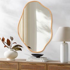 a white vase sitting on top of a wooden table next to a mirror and lamp