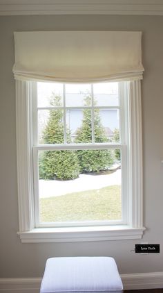 a window with a white bed in front of it and a small bench under the window