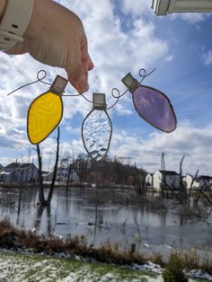 a hand is holding three christmas lights in front of a frozen lake