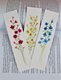 three bookmarks with flowers painted on them sitting on top of an open book page