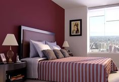 a bedroom with red walls and striped bedspread in front of a large window