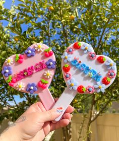 two heart shaped lollipops decorated with flowers and strawberries are held in front of a tree