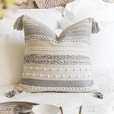 a pillow with tassels on it sitting on a bed next to a cup