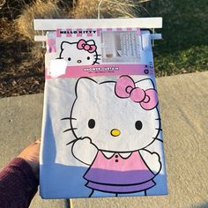 a hello kitty notebook is being held up by someone's hand on the sidewalk