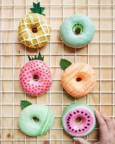 four donuts with different colors and designs are on a wire rack next to pineapples