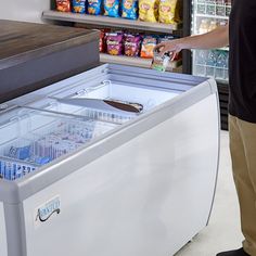 a man standing in front of a freezer filled with drinks and snacks next to a refrigerator