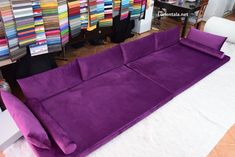 a large purple couch sitting on top of a white floor next to a pile of clothes