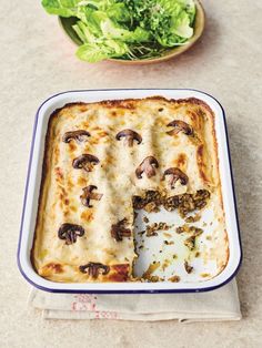 a casserole dish with broccoli and mushrooms in it next to a bowl of lettuce