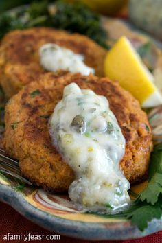 two crab cakes on a plate with lemon wedges