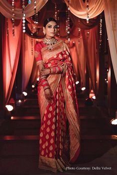 a woman in a red and gold sari standing under an archway with lights on either side