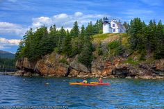 two people in kayaks paddling towards a lighthouse on a cliff near the ocean