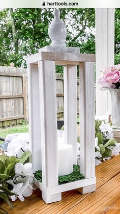 a white lantern sitting on top of a wooden table next to a vase filled with flowers