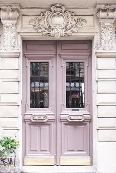 an old building with two pink doors and some flowers on the sidewalk in front of it