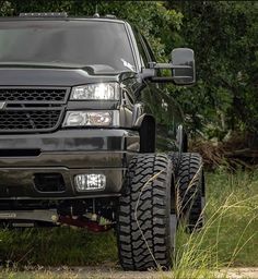 the front end of a black truck parked on a dirt road near grass and trees