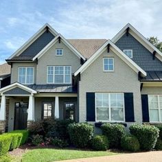 a gray house with black shutters on the front and side windows, bushes in front