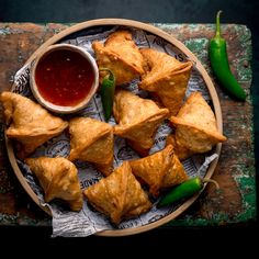 several pastries on a plate with dipping sauce and green chili peppers next to them