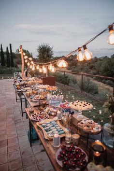 a long table filled with lots of food on top of a wooden table covered in lights