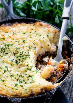 a casserole with meat and vegetables in it on a wooden table next to parsley