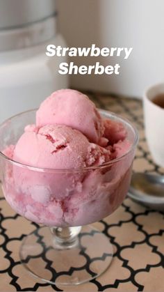 two scoops of strawberry sherbet sit in a glass bowl next to an ice cream maker