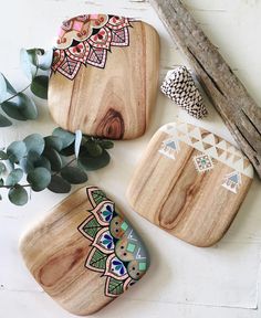 three wooden trays with designs on them next to some leaves and branches, one has a plant in it