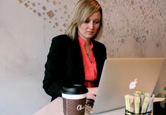 a woman sitting at a table with a laptop and coffee cup in front of her