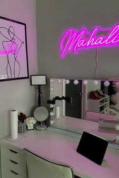 a desk with a mirror, laptop and lights on it in front of a pink wall