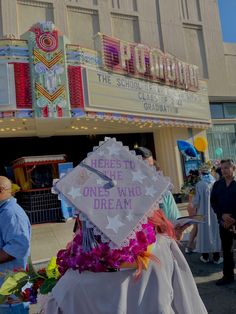 a person wearing a graduation cap with flowers in front of a movie theater and people standing around