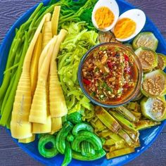 an assortment of vegetables on a blue plate with eggs and sauce in the middle, including celery