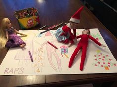 two elf dolls sitting on top of a table next to crayons and markers