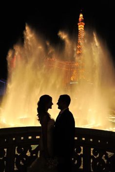 a bride and groom standing in front of a fountain at night