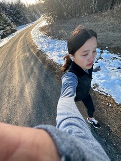 a person holding the hand of another person on a road with snow and trees in the background