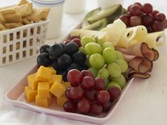 grapes, cheese and other fruits are arranged on a plate next to a basket of crackers