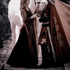 a man and woman dressed in medieval clothing standing next to a white horse