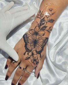 a woman's hand with a butterfly tattoo on it and flowers around the wrist