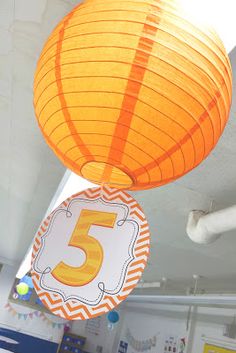 an orange paper lantern hanging from the ceiling in a room with tables and desks