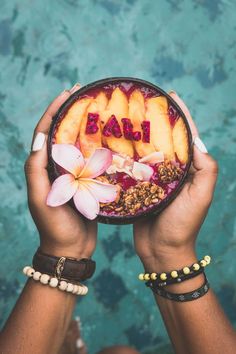 a person holding up a bowl with fruit and flowers on it that says, bali