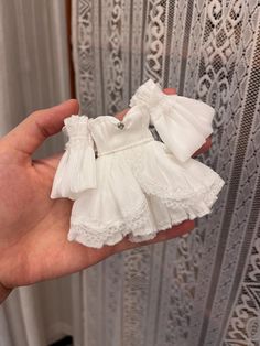 a hand holding a small white dress with ruffles on it's sleeves