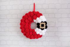 a red and white knitted wreath hanging on a brick wall next to a candle