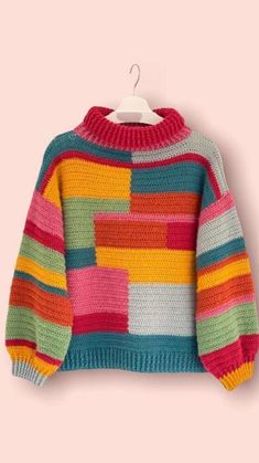 a multicolored sweater hanging on a hanger against a pink wall with a white background