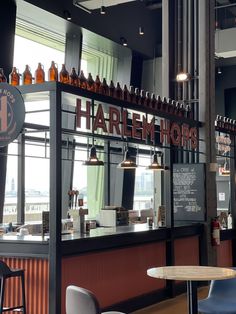 the interior of a restaurant with tables and stools in front of windows that have beer bottles on them