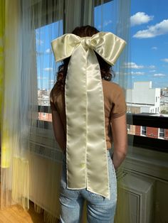 a woman standing in front of a window with a large bow on her head and back