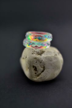 a rock with a ring on it sitting in front of a black background that has an iridescent effect