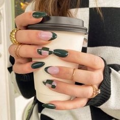 a woman holding a coffee cup with green and white nail polish on her nails, while wearing gold rings