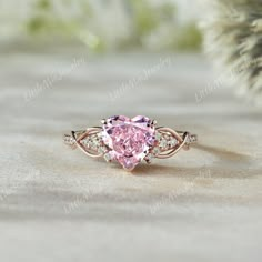 a pink heart shaped diamond ring with three diamonds on the band and side stones around it